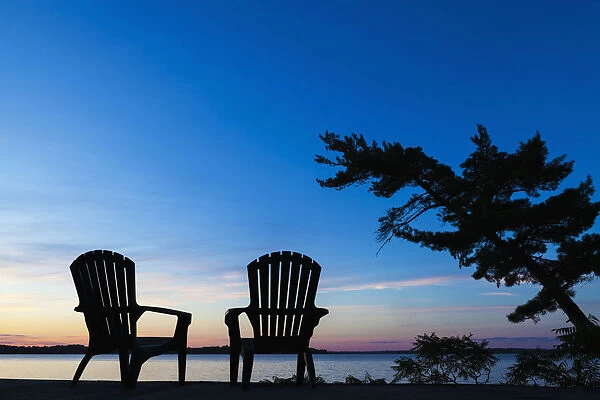 Silhouette Of Muskoka Chairs And Balsam Lake At Sunrise; Ontario, Canada