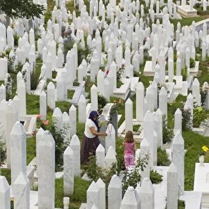 Muslim woman and child tend a grave at a war cemetery, Sarajevo, Bosnia