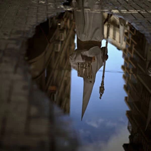 A penitent is reflected in a puddle of water after rain fell at the Humildad brotherhood
