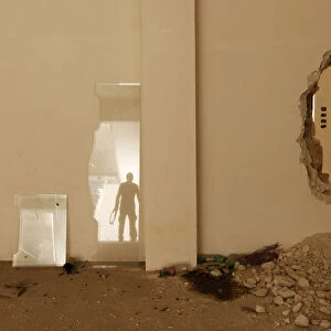 The reflection of a Free Syrian Army fighter carrying his weapon is seen on a glass pane
