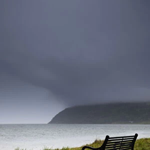 A bench at the waters edge with a dark stormy sky; Moray firth scotland